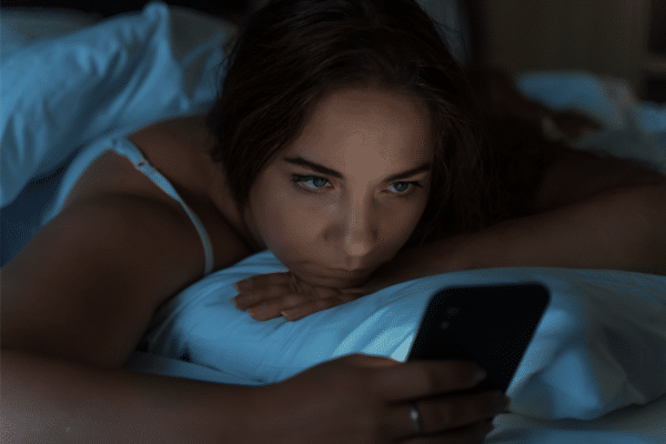 Woman awake in bed looking at her smartphone - Dopamine fasting.
