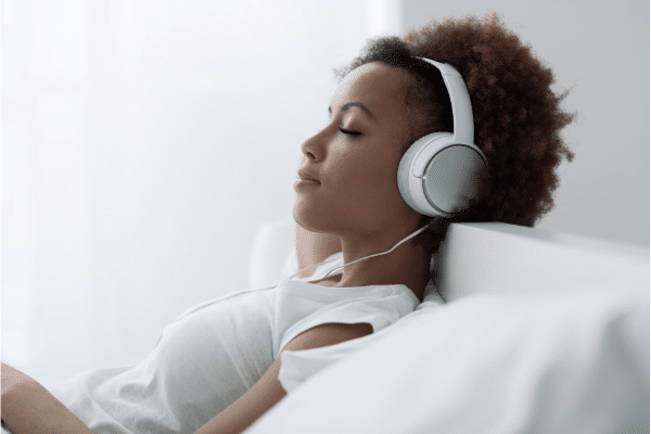 Woman laying back on sofa, breathing deeply, wearing headphones.